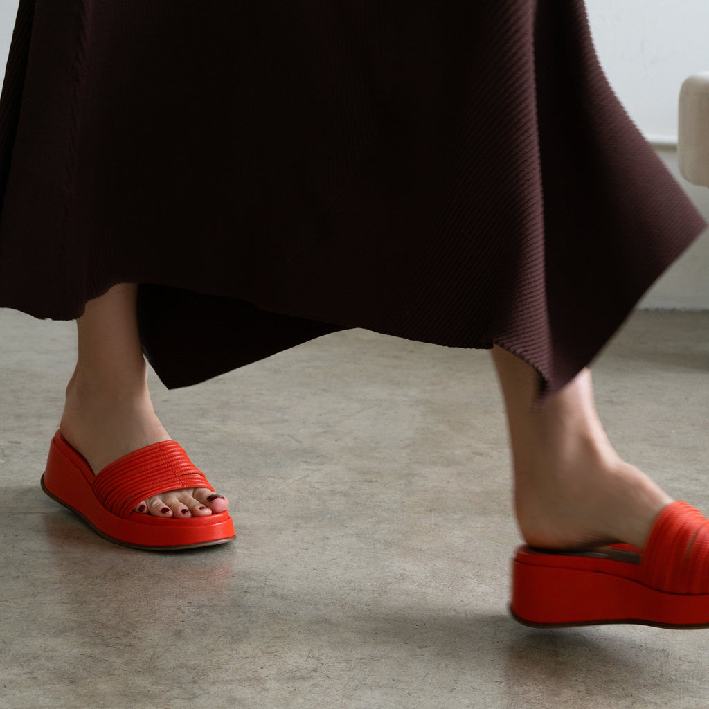 Close-up of a foot in a red fabric wedge sandal on a textured gray floor.