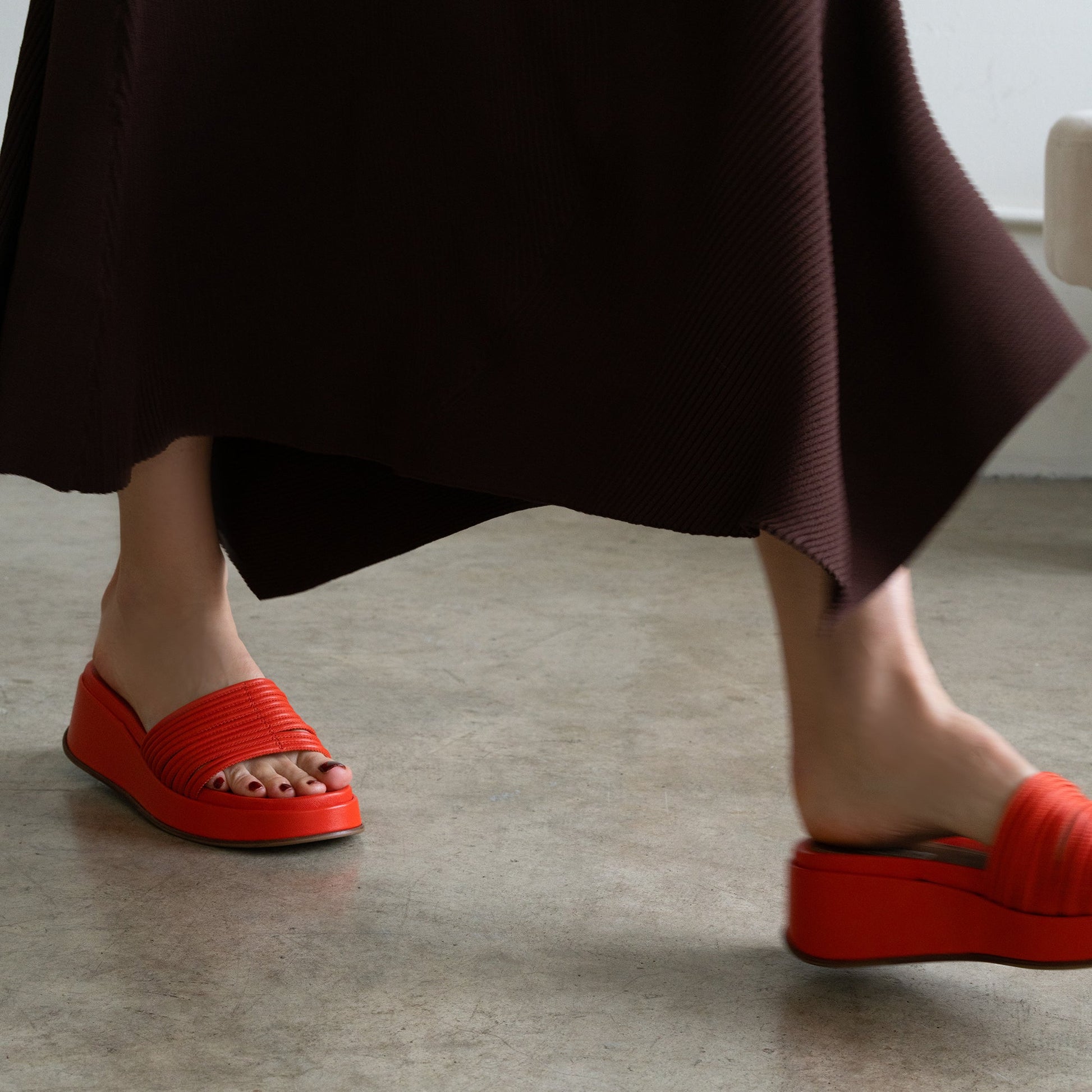 Close-up of a foot in a red fabric wedge sandal on a textured gray floor.