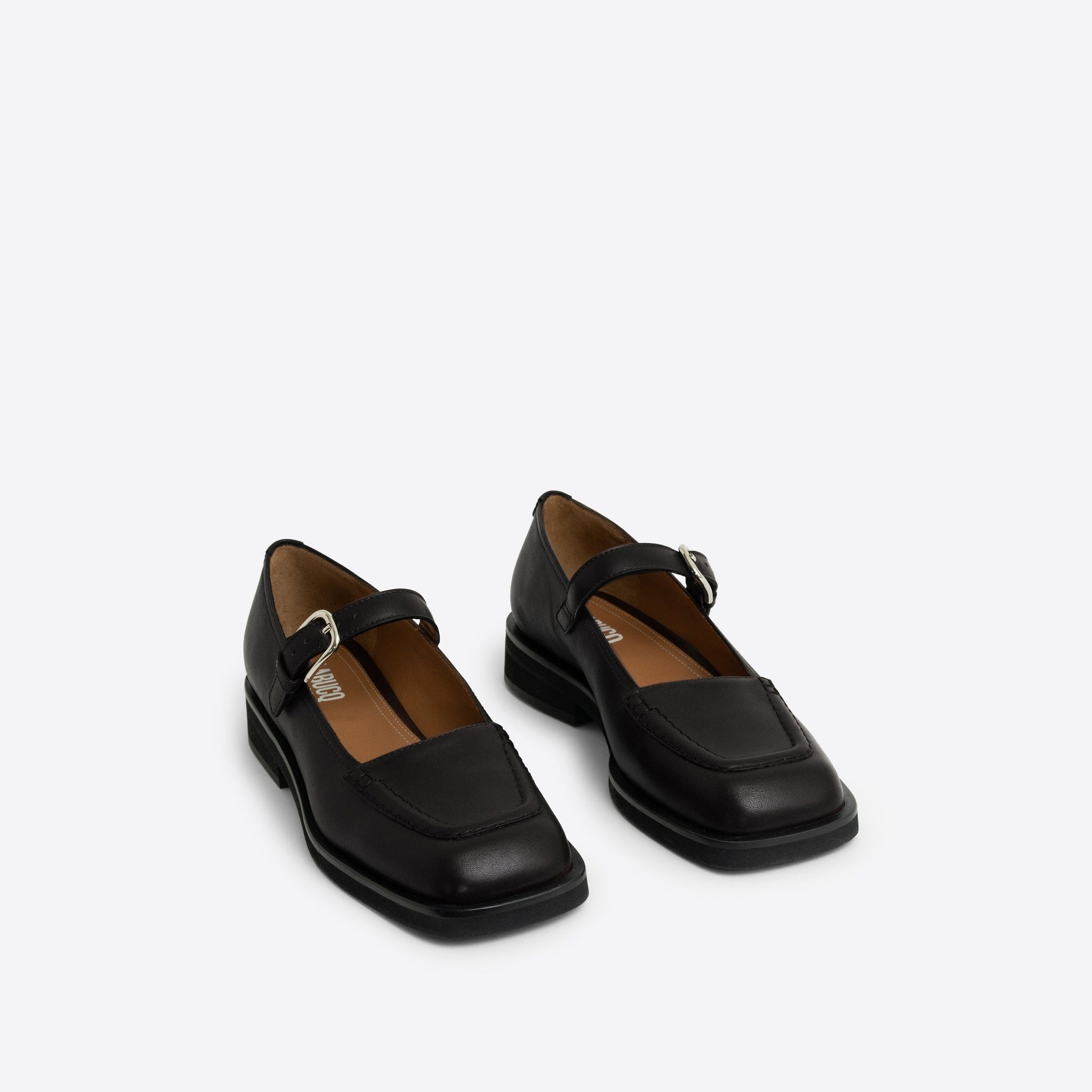 Pair of black Maryjanes with a black sole and a buckle on a white background