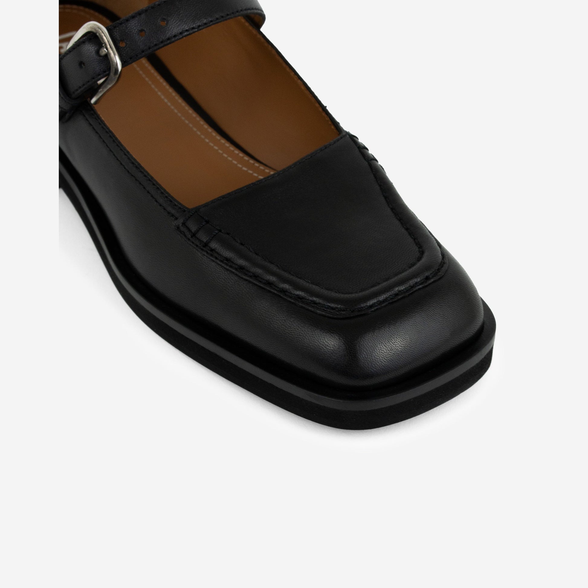 Close-up of black Maryjanes with a black sole and a buckle on a white background