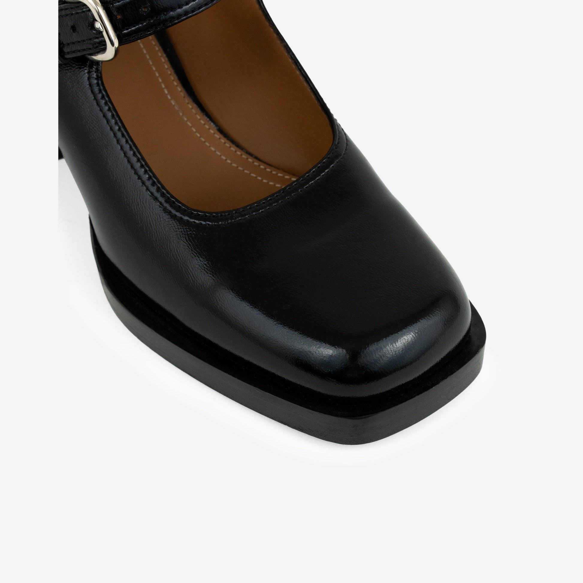 Close-up shot of black patent leather Maryjanes with a buckle, and a black sole on a white background