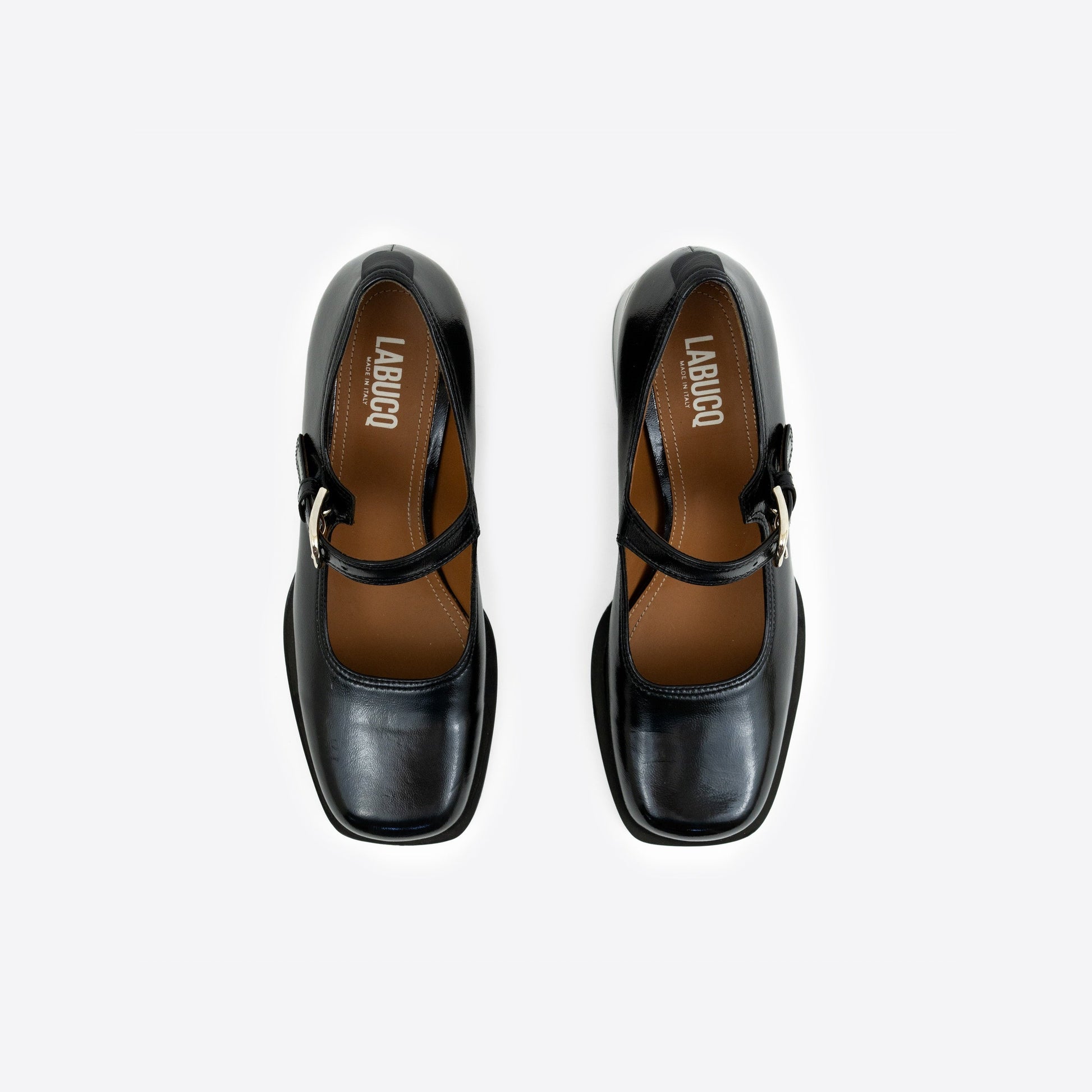 Top-view shot of a pair of black patent leather Maryjanes with visible Labucq branding, a buckle and a black sole on a white background