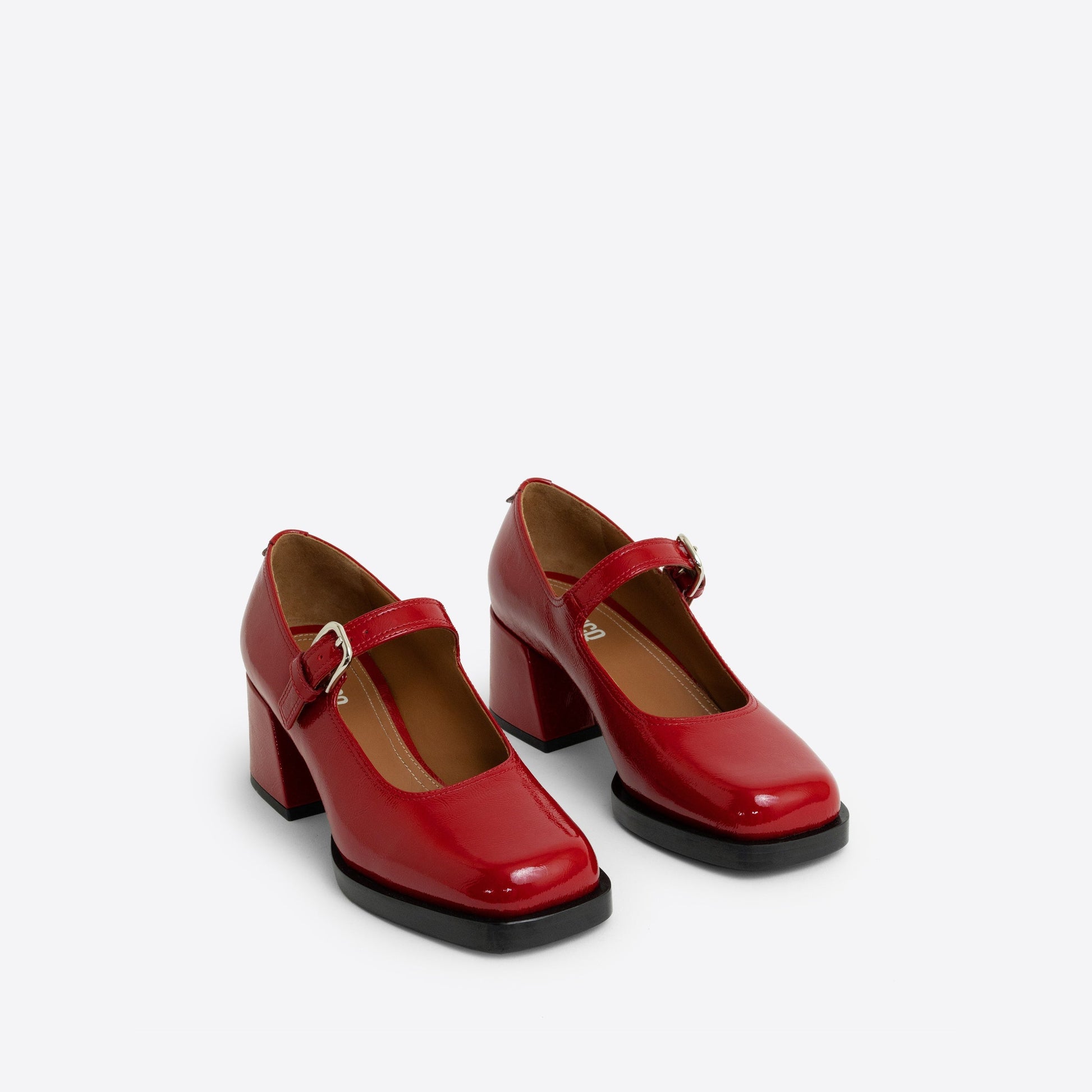 Pair of red patent leather Maryjanes with a buckle and a black sole on a white background