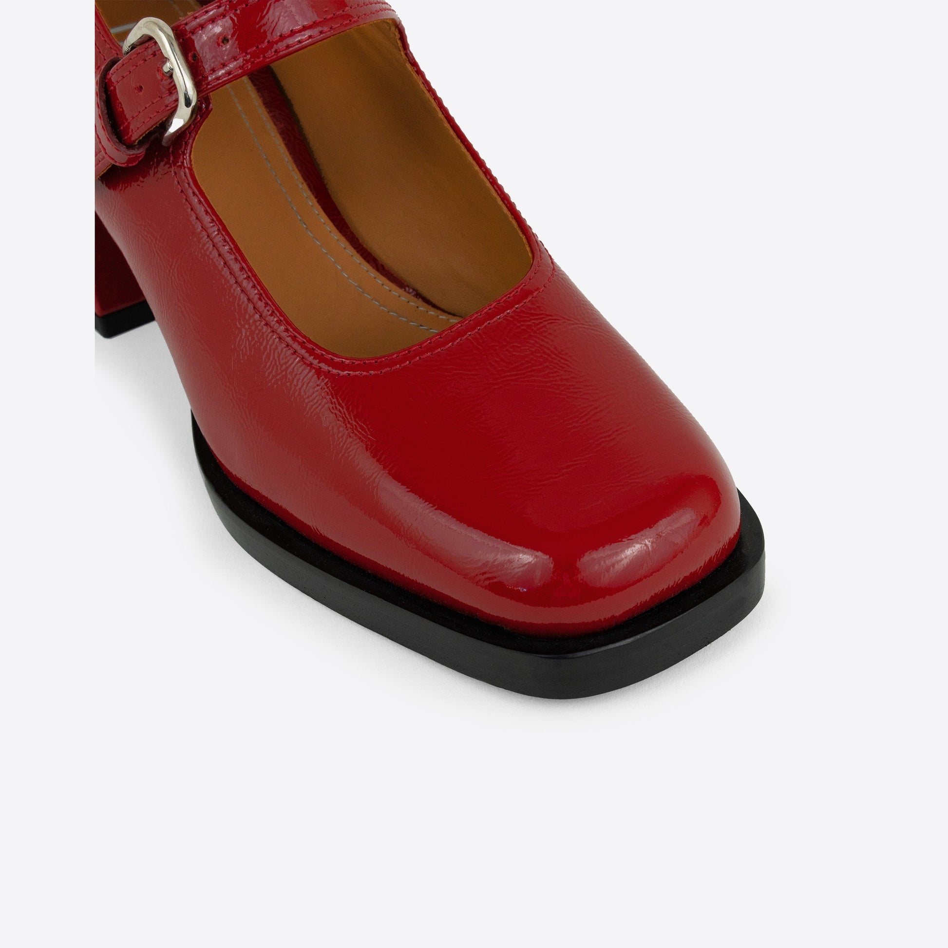 Close-up shot of red patent leather Maryjanes with a buckle and a black sole on a white background