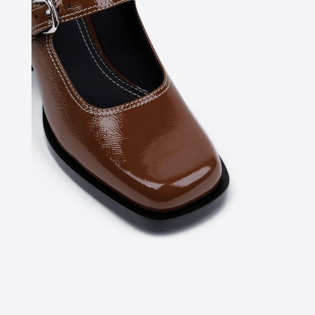 Close-up of a brown patent leather shoe with a black sole on a white background