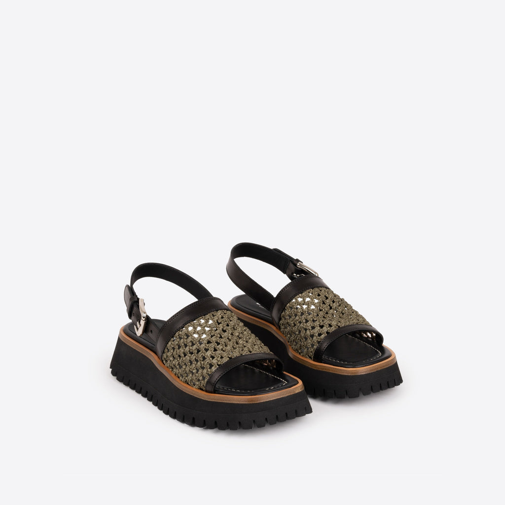 Pair of black platform sandals with brown lining and an olive woven raffia strap on a white background