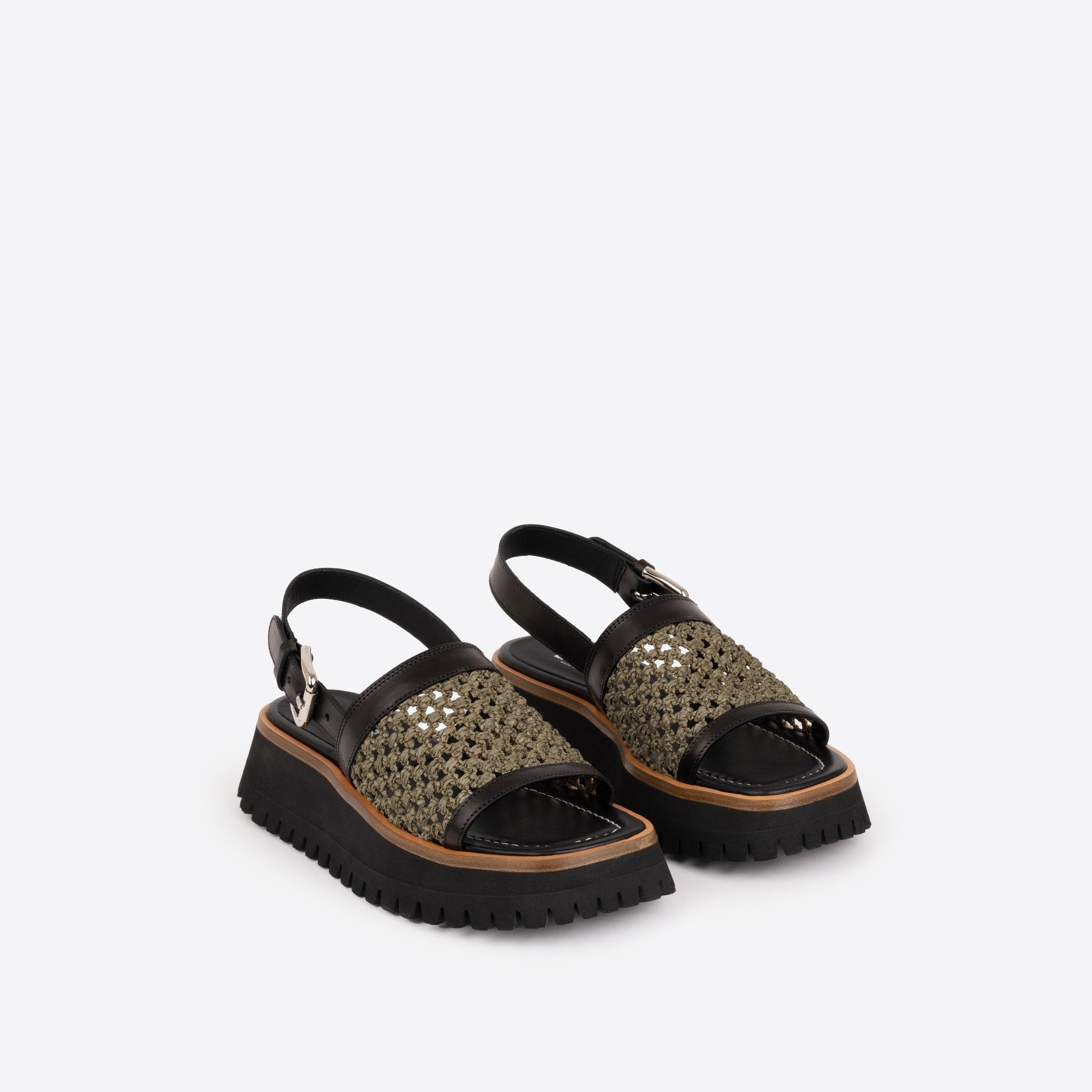 Pair of black platform sandals with brown lining and an olive woven raffia strap on a white background