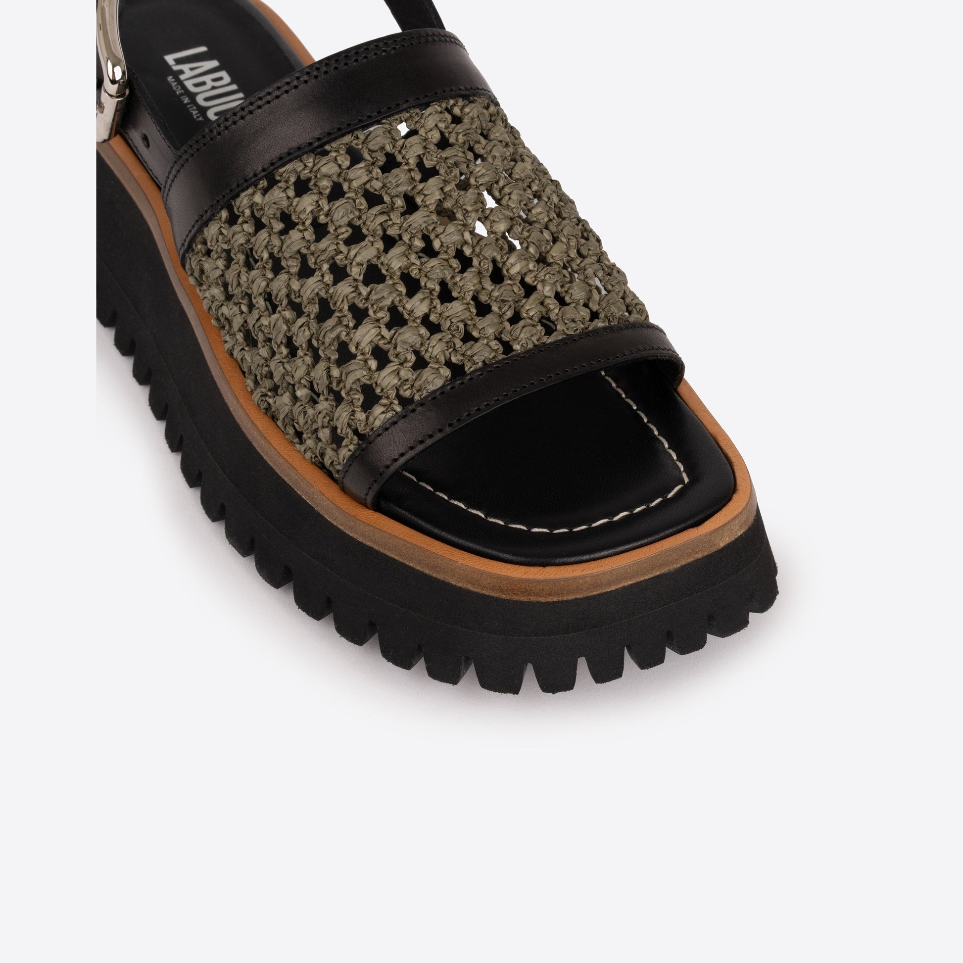 Black platform sandal with brown lining and an olive woven raffia strap on a white background