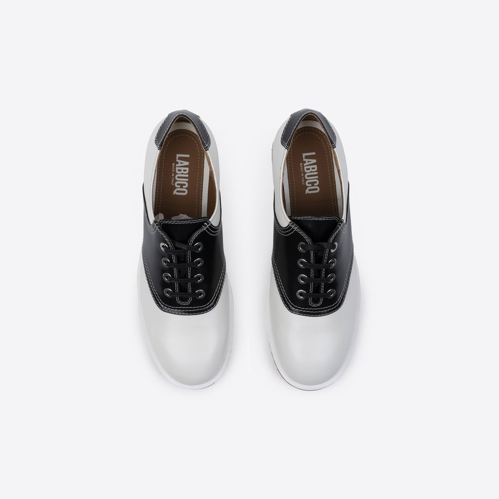 Pair of white and black leather shoes featuring the Labucq logo, with black laces and a brown sole on a white background