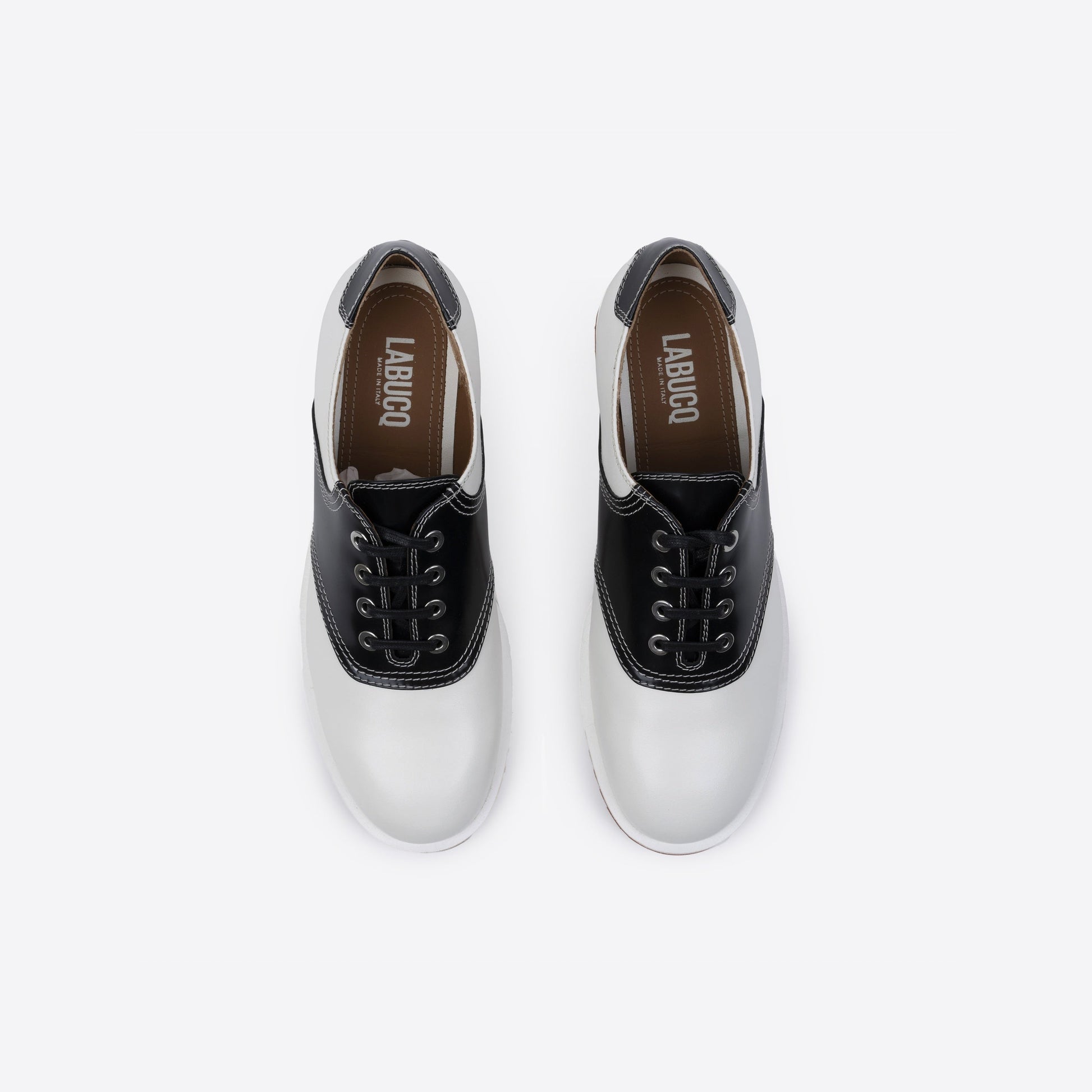 Pair of white and black leather shoes featuring the Labucq logo, with black laces and a brown sole on a white background