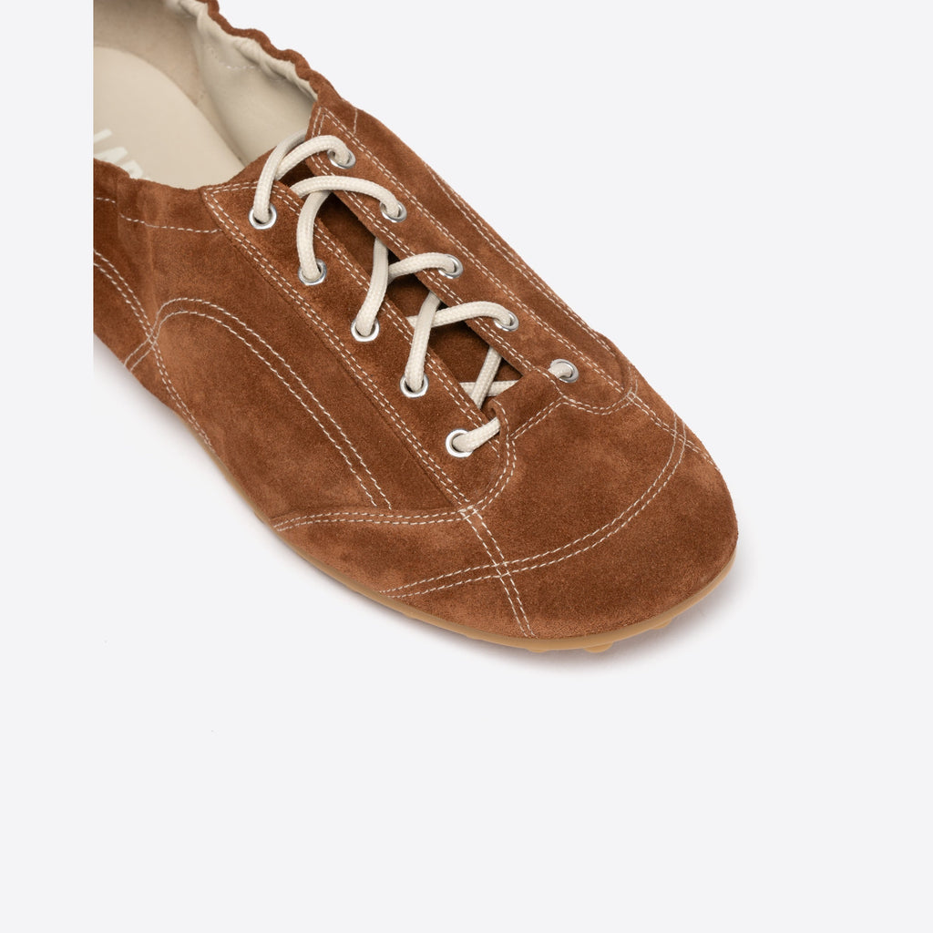 Brown suede shoe with white laces on a light gray background