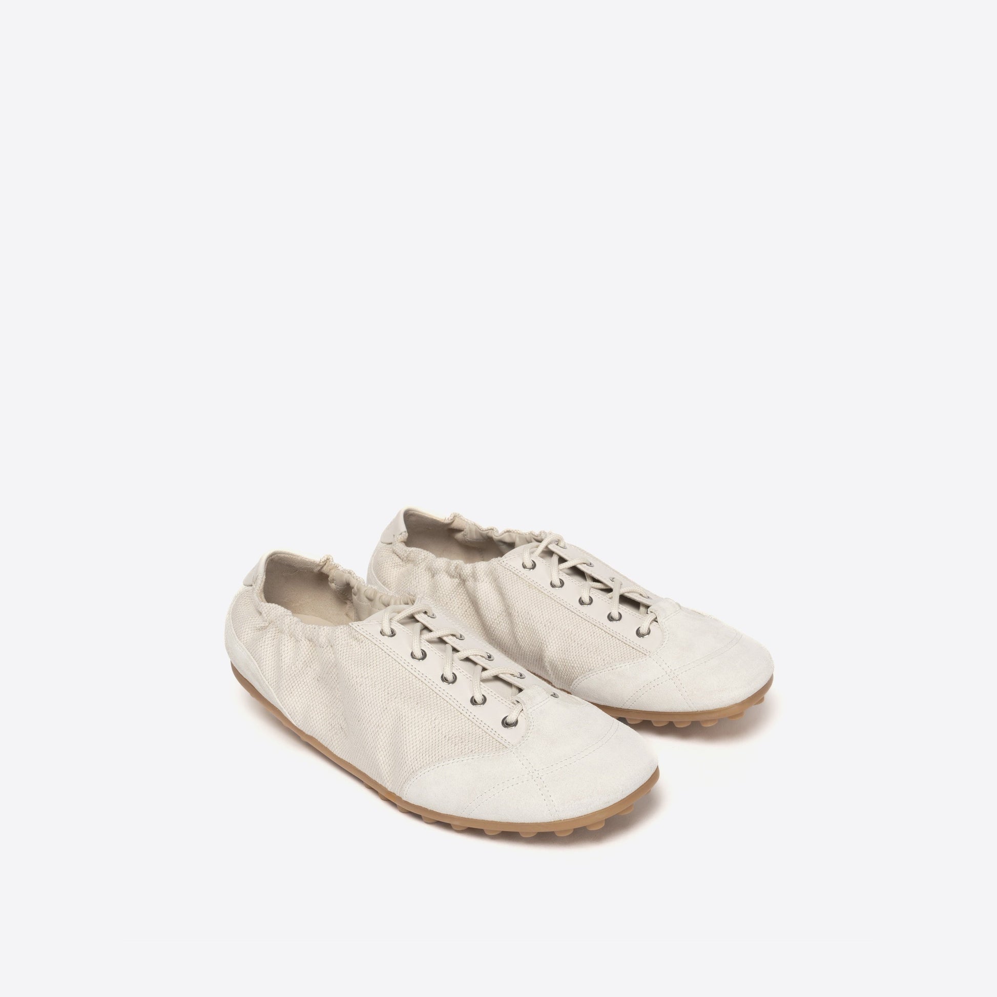 Pair of white shoes with light brown sole on a light beige background