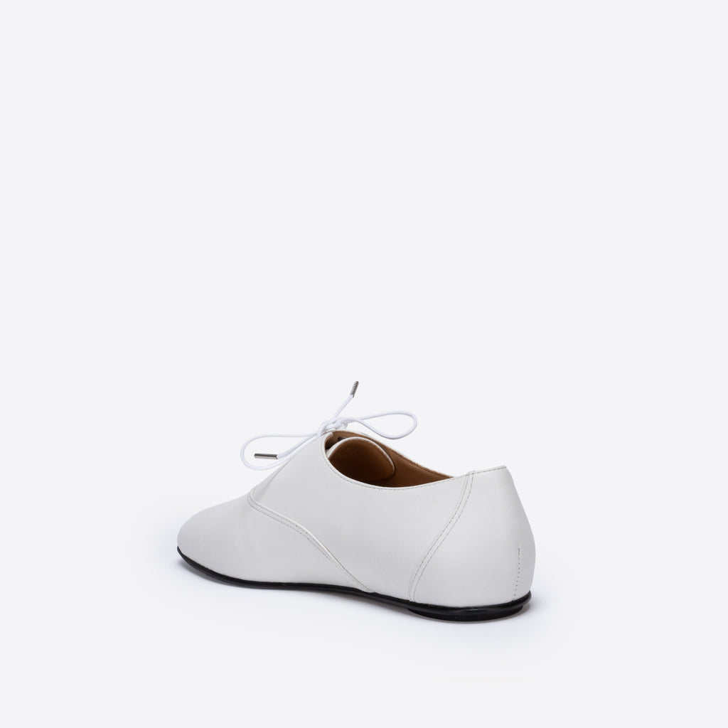 White leather shoes with white laces that have silver aglets on a white background